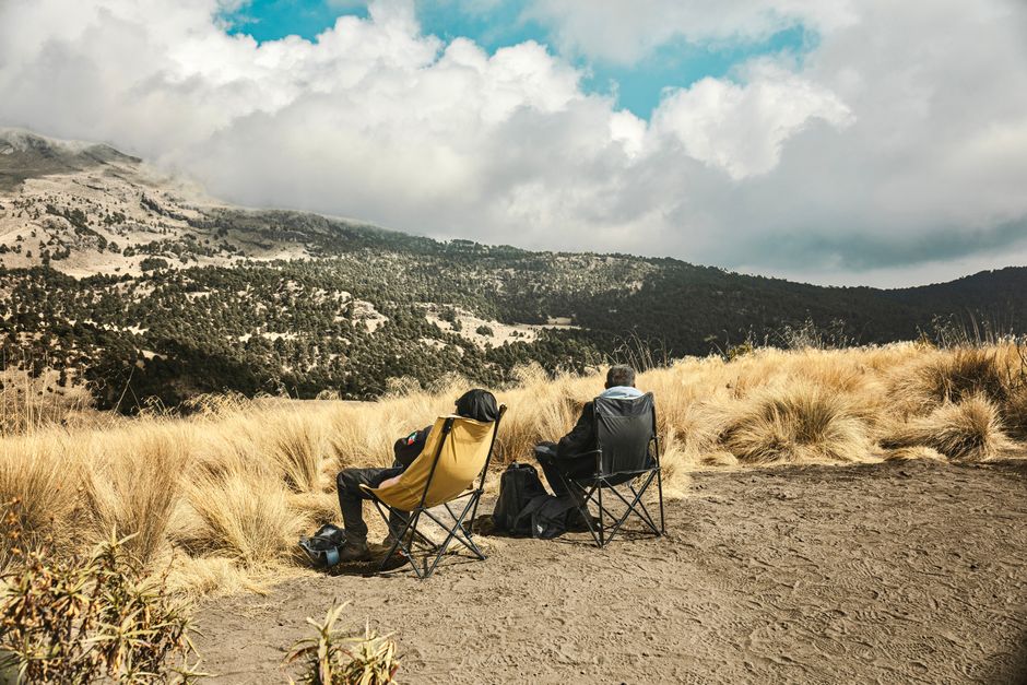 Two hikers sitting in chairs enjoy a scenic mountain view under a cloudy sky.
