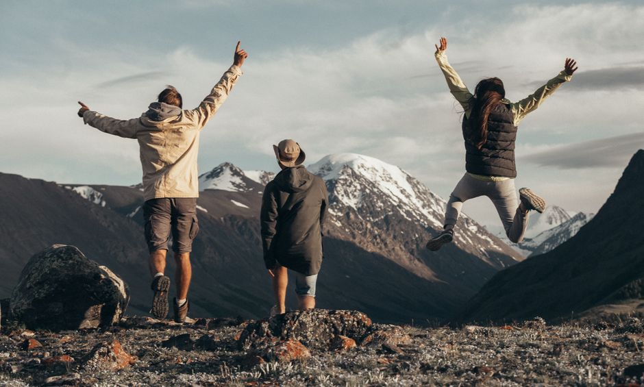 Three people enjoying a hike in snow-capped mountains, jumping with joy filled with adventure.