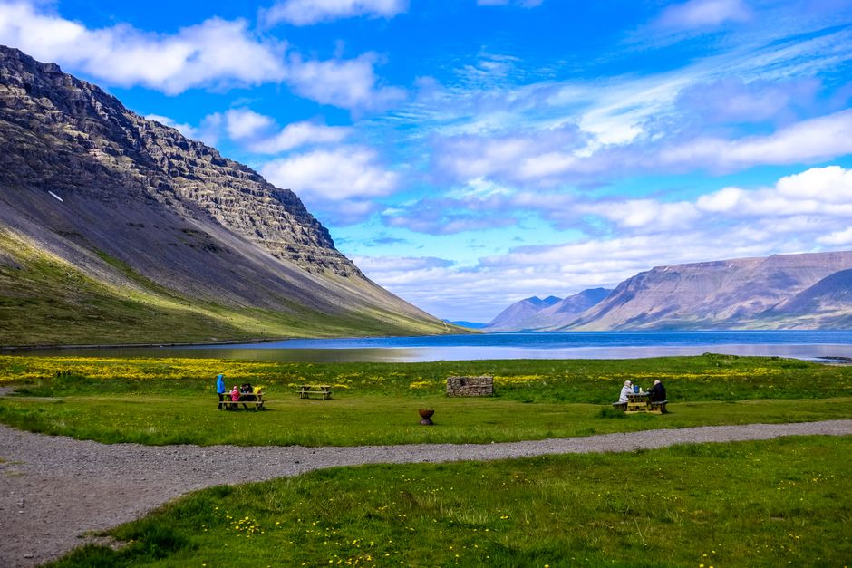 Breathtaking view of a grassy field, lake, and mountains under a bright blue sky.