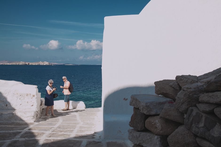 Tourists enjoy a sunny day by the sea in Mykonos, Greece, surrounded by iconic white architecture.